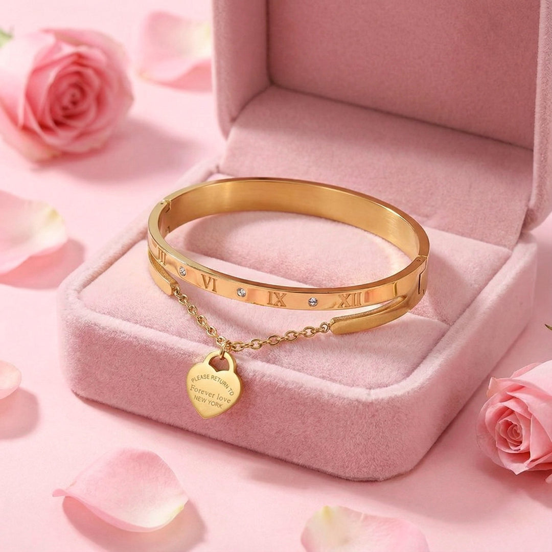 Gold bracelet with a heart charm on a pink jewelry box with pink roses in the background